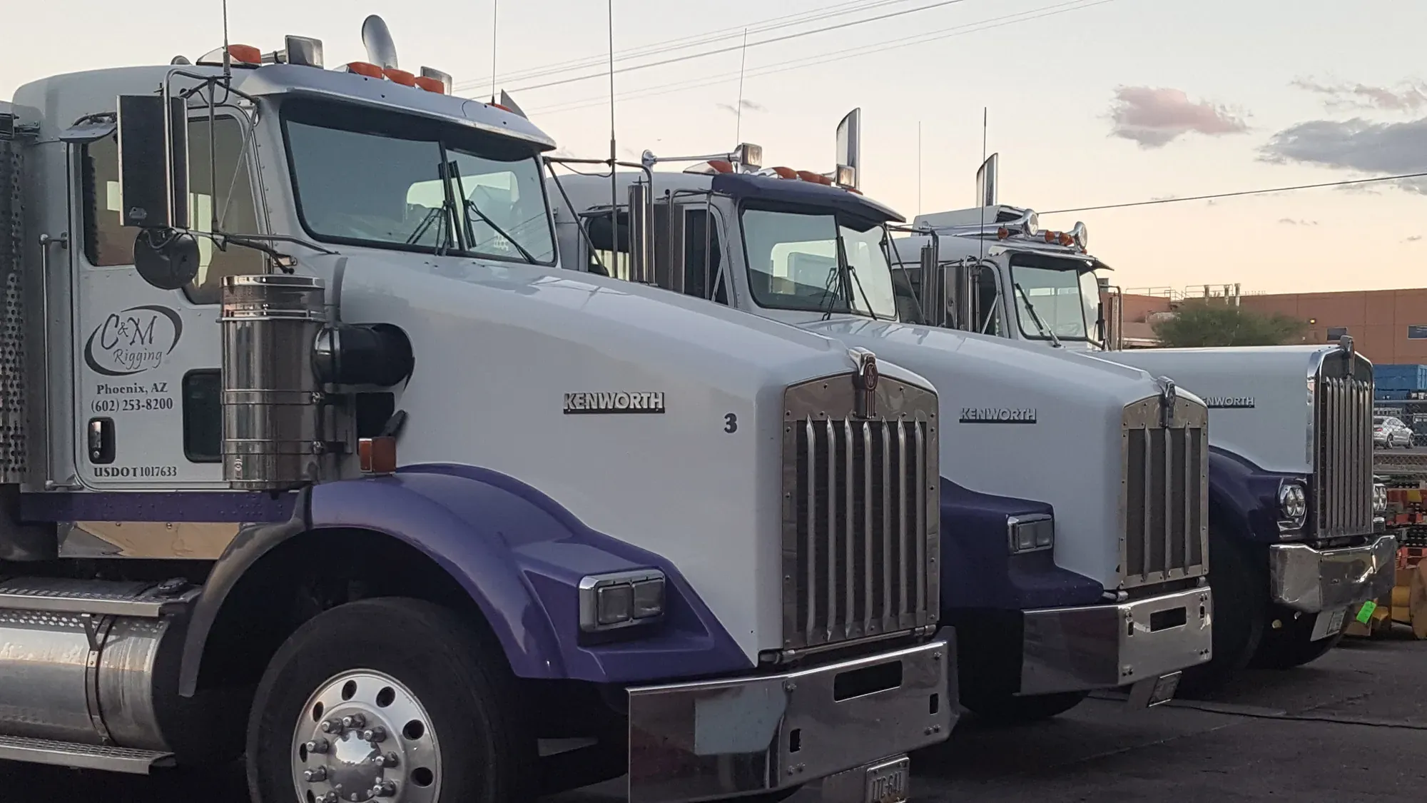 Close-up of three C&M Rigging Kenworth tractors parked nose-to-nose at dusk, showing the C&M Rigging door decal, Phoenix phone number, and USDOT 1017633.